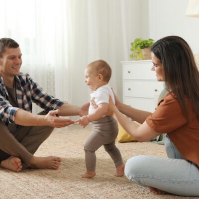 Young couple helping child take their first steps in a new home