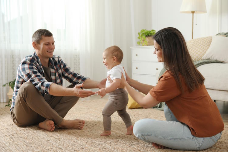 Young couple helping child take their first steps in a new home 